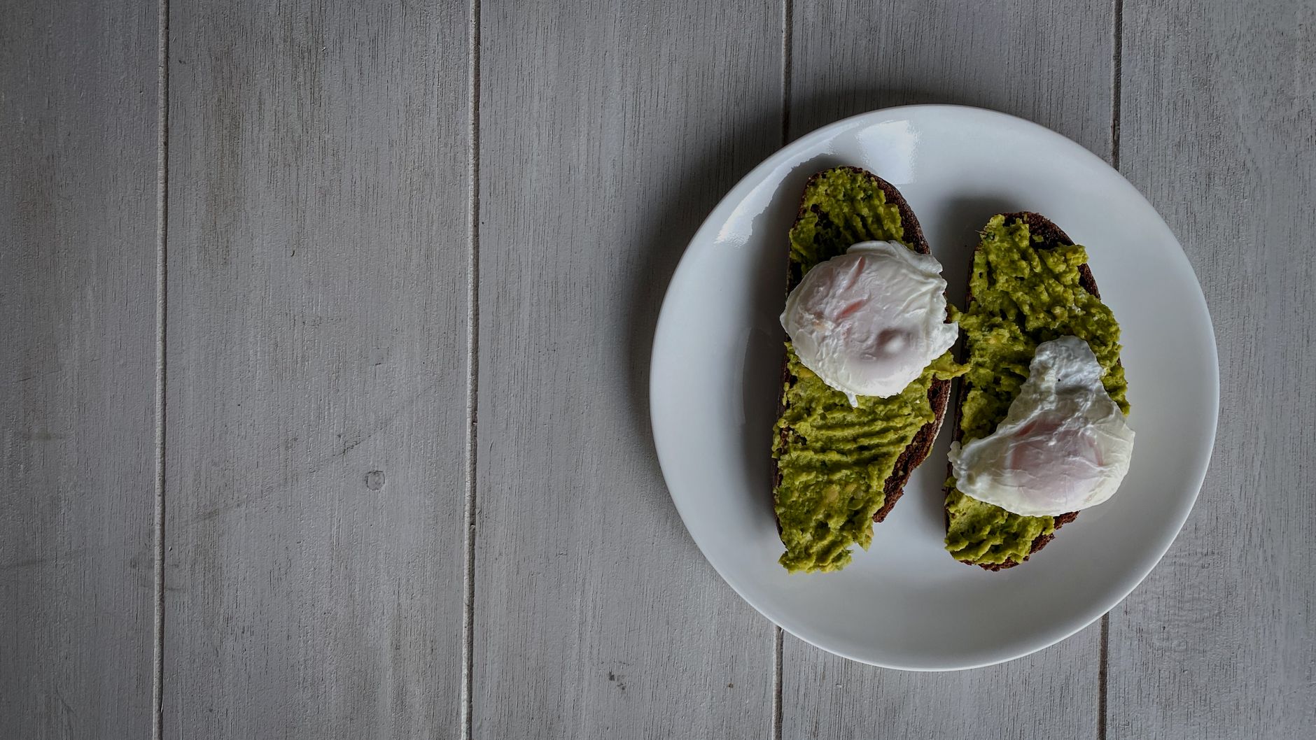 Avocado toast with two poached eggs and red pepper flakes on dark sourdough
