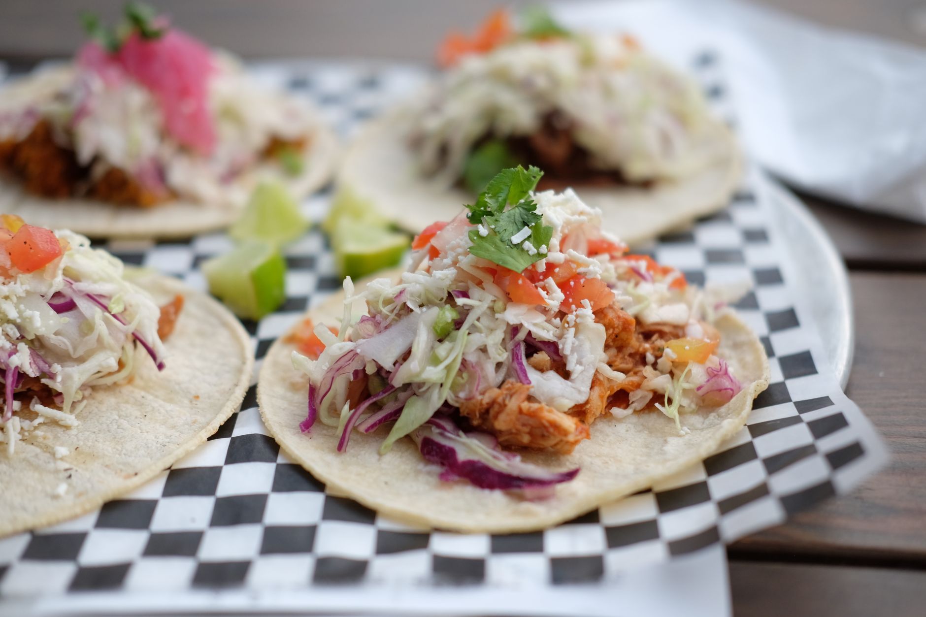 Blackened chicken tacos with purple cabbage slaw and avocado crema on dark wooden board