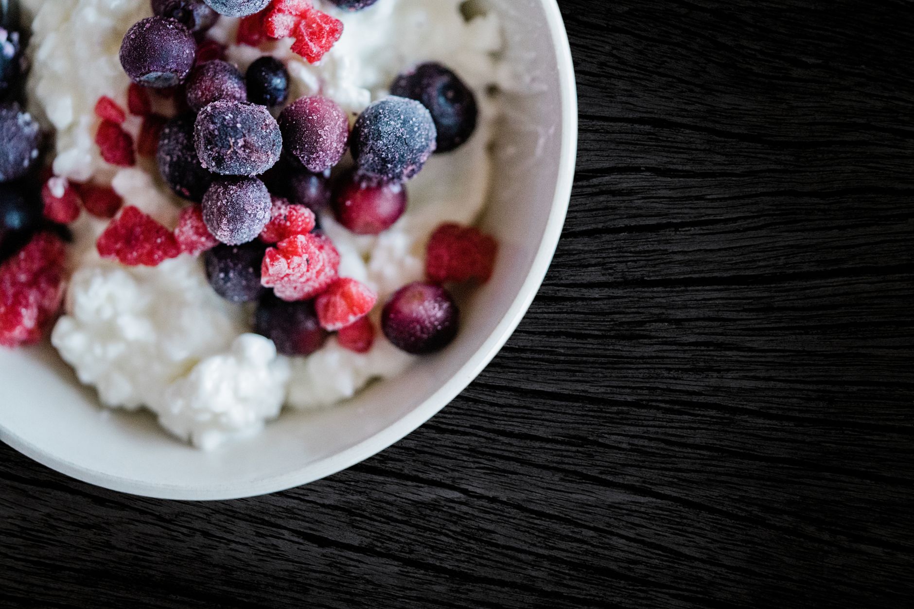 Cottage cheese fruit bowl with strawberries, blueberries and honey in dark ceramic bowl