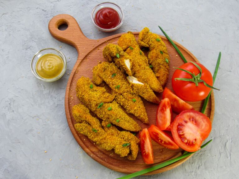 Crispy golden baked chicken tenders with dipping sauce on dark slate