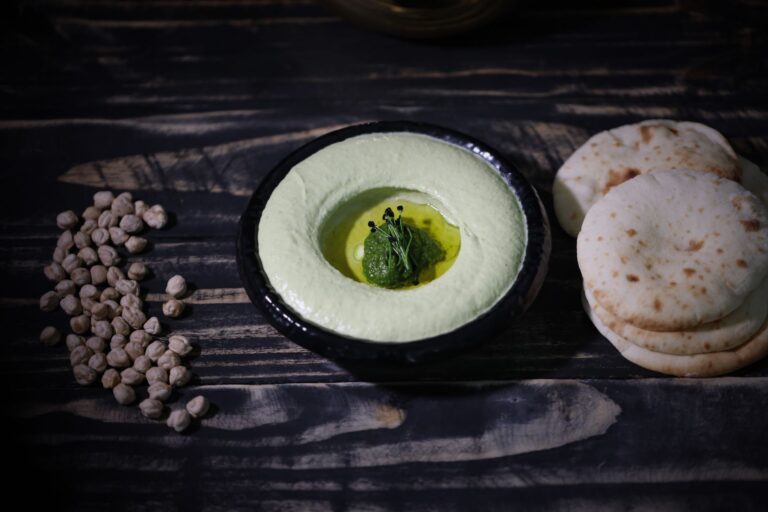 Bright green edamame hummus in dark bowl with olive oil and sesame seeds