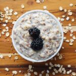 High-protein overnight oats in glass jar with berries and chia seeds on dark background