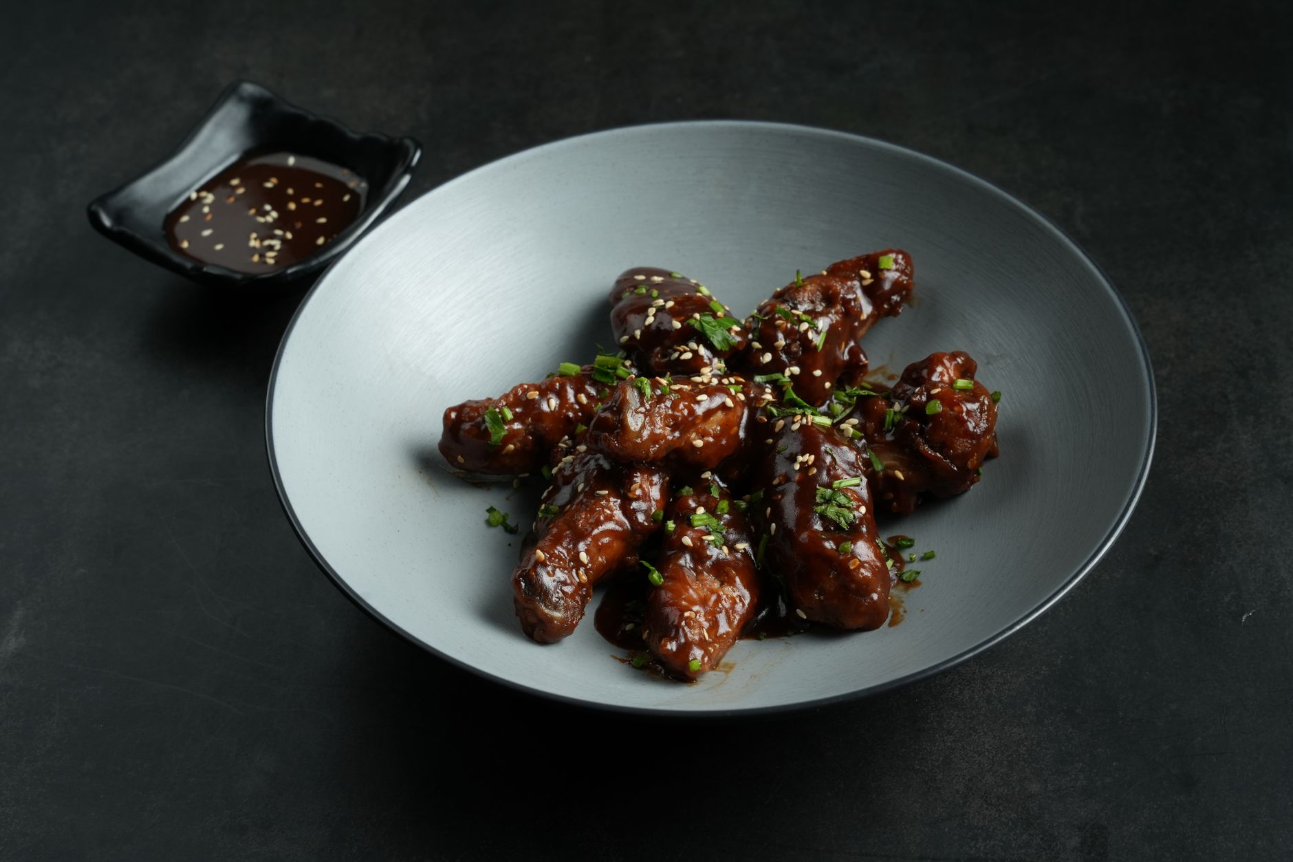 Honey sriracha glazed chicken thighs with sesame seeds and green onions on dark plate