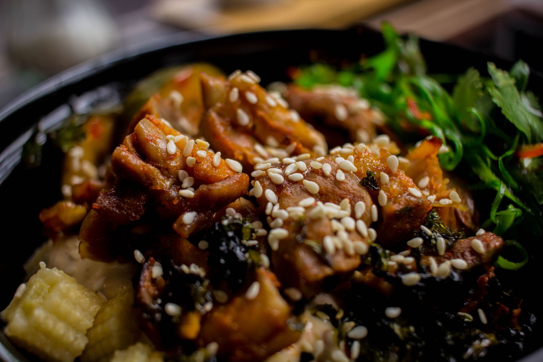 Smashed cucumber chicken bowl with sesame dressing and chili oil over rice in dark bowl