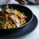 Teriyaki salmon bowl with rice, edamame and sesame seeds in dark ceramic bowl