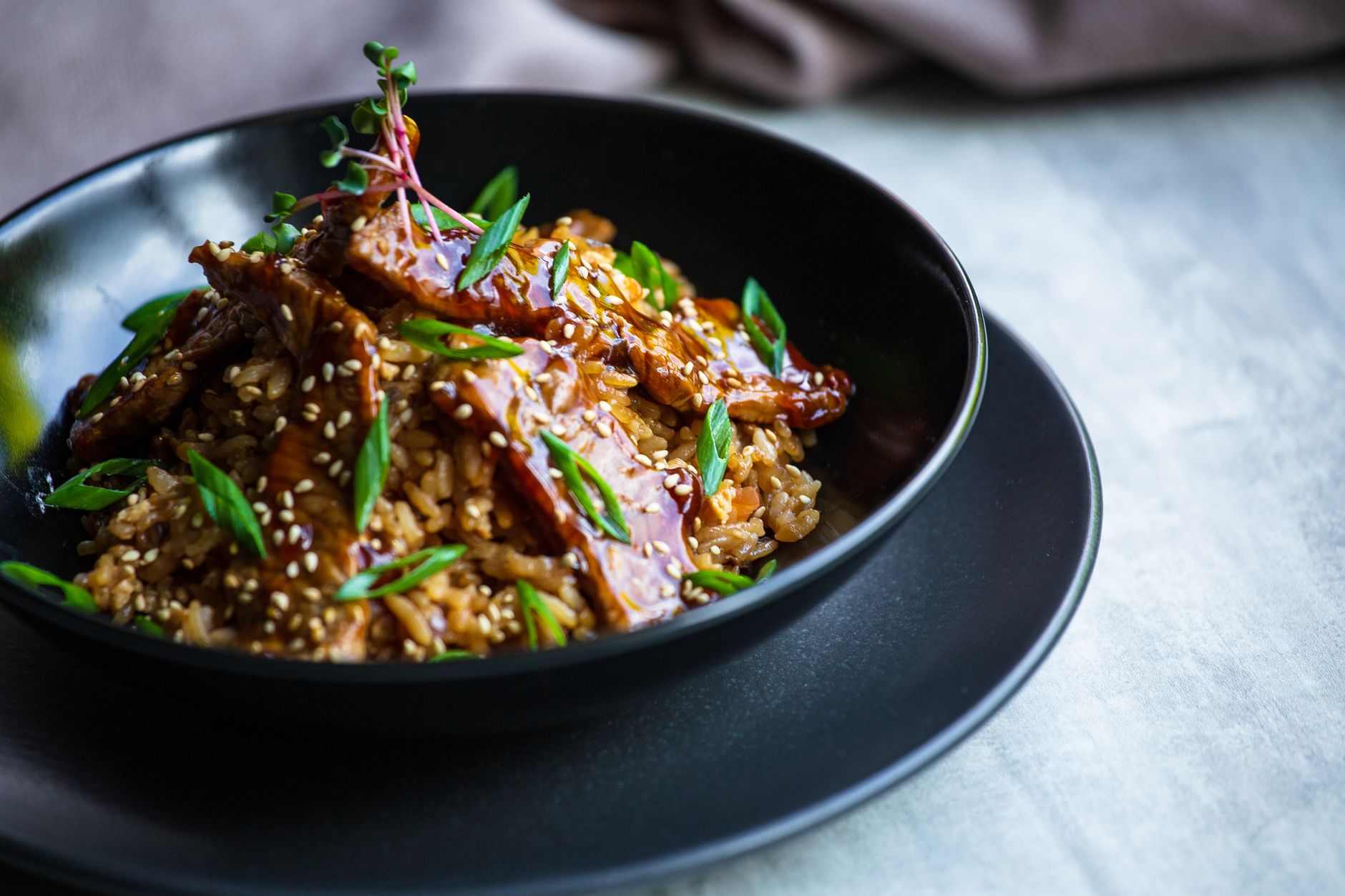 Teriyaki salmon bowl with rice, edamame and sesame seeds in dark ceramic bowl