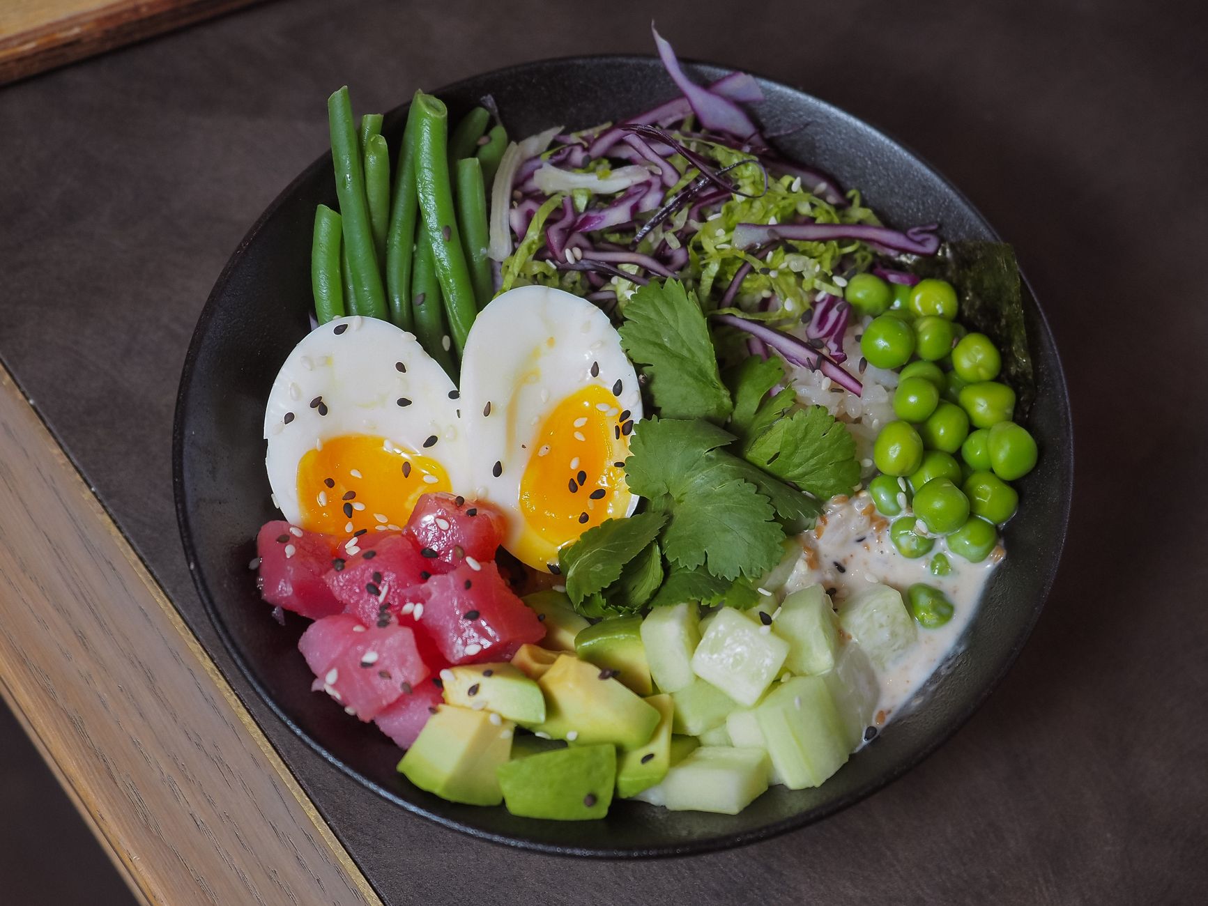 Tuna avocado rice bowl with edamame and sesame seeds in dark ceramic bowl